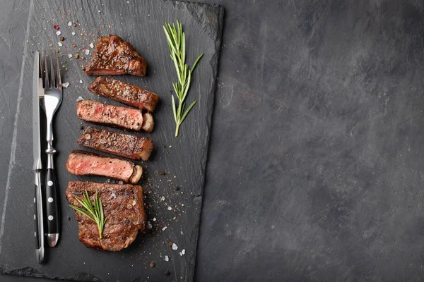 Gros plan prêt à manger steak New York races de bœuf d'Angus noir avec des herbes, de l'ail et du beurre sur une planche de pierre. Le plat fini pour le dîner sur un fond de pierre sombre. Vue supérieure avec espace de copie — Photo