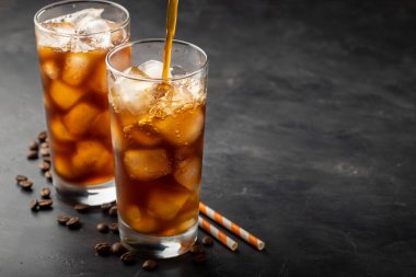 Buzlu kahve üzerinden uzun bir cam ve kahve çekirdekleri bir eski rustik ahşap tablo. Kopya alanı ile karanlık bir arka plan üzerinde soğuk yaz içeceği. Bir bardak içine bir kahve kabı üzerinden dökülen içki süreci.