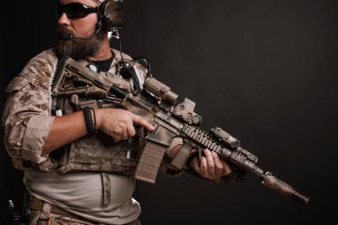 Acımasız adam askeri çöl üniforma ve vücut zırh mücadele bir rafa anlamına gelir ve bir siyah arka plan üzerine tüfeğini tutar. Amaçlayan bir tüfek airsoft koruyucu gözlük sakallı Player'da.