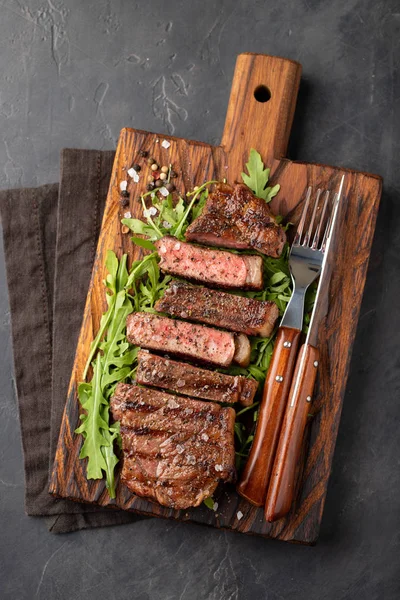 Gros plan prêt à manger steak New York races de bœuf d'Angus noir avec des herbes, de l'ail et du beurre sur une planche de bois. Le plat fini pour le dîner sur un fond de pierre sombre. Vue du dessus — Photo