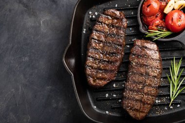 Closeup biftek üst bıçak sığır ırkları siyah yemeye hazır Angus ile ızgara domates, sarımsak ve ahşap bir gemide. Bitmiş çanak taş karanlık bir arka plan akşam yemeği için. Kopya alanı ile üstten görünüm
