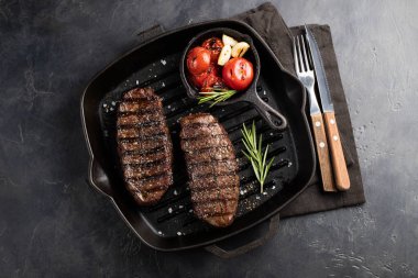 Closeup biftek üst bıçak sığır ırkları siyah yemeye hazır Angus ile ızgara domates, sarımsak ve ahşap bir gemide. Bitmiş çanak taş karanlık bir arka plan akşam yemeği için. Üstten görünüm.