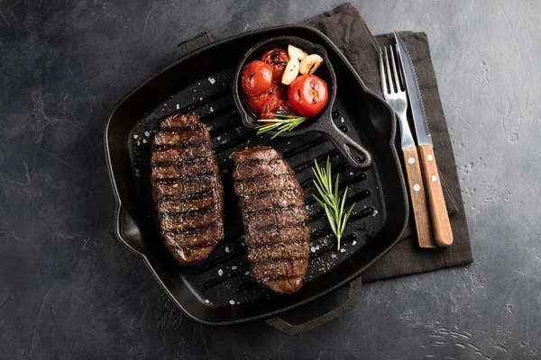 Closeup biftek üst bıçak sığır ırkları siyah yemeye hazır Angus ile ızgara domates, sarımsak ve ahşap bir gemide. Bitmiş çanak taş karanlık bir arka plan akşam yemeği için. Üstten görünüm.