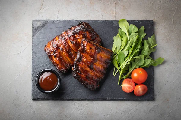 Domuz kaburga closeup Barbekü sosu ve roka ile ızgara. Lezzetli Aperatif bir taş Yönetim Kurulu eski beton zemin üzerine doldurmak için bira için. Üstten görünüm.