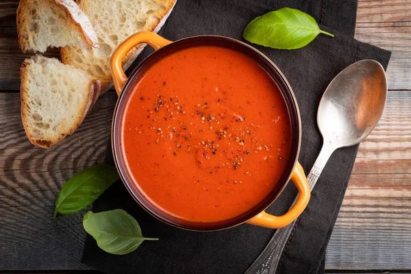 Fesleğen, ekmek ve zeytinyağı ahşap bir masa üzerinde ev yapımı domates çorbası. Karanlık bir arka plan üzerinde bir vejetaryen tabağı hazırladı. Üstten görünüm.