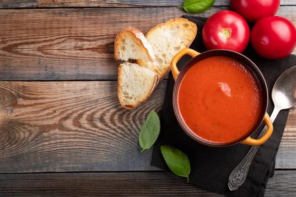 Fesleğen, ekmek ve zeytinyağı ahşap bir masa üzerinde ev yapımı domates çorbası. Karanlık bir arka plan üzerinde bir vejetaryen tabağı hazırladı. Kopya alanı ile üstten görünüm.