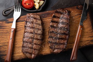 Closeup biftek üst bıçak sığır ırkları siyah yemeye hazır Angus ile ızgara domates, sarımsak ve ahşap bir gemide. Bitmiş çanak taş karanlık bir arka plan akşam yemeği için. Üstten görünüm