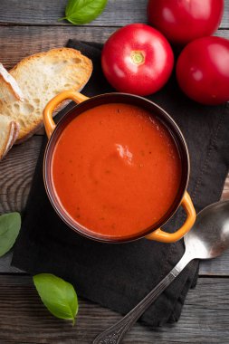 Fesleğen, ekmek ve zeytinyağı ahşap bir masa üzerinde ev yapımı domates çorbası. Karanlık bir arka plan üzerinde bir vejetaryen tabağı hazırladı. Üstten görünüm