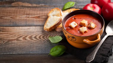 Fesleğen, ekmek ve zeytinyağı ahşap bir masa üzerinde ev yapımı domates çorbası. Karanlık bir arka plan üzerinde bir vejetaryen tabağı hazırladı. kopya alanı ile