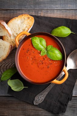 Fesleğen, ekmek ve zeytinyağı ahşap bir masa üzerinde ev yapımı domates çorbası. Karanlık bir arka plan üzerinde bir vejetaryen tabağı hazırladı. Üstten görünüm