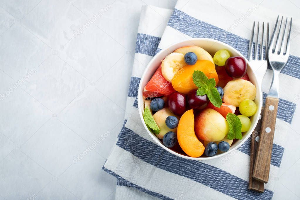 Bowl of healthy fresh fruit salad on a white background. Top view with copy space. Flat lay.