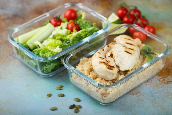 Healthy meal prep containers with quinoa, chicken breast and green salad overhead shot.