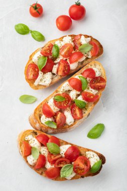 Bruschetta domates, mozzarella peyniri ve fesleğen üzerinde hafif bir arka plan ile. Geleneksel İtalyan meze veya aperatif, meze. Üstten görünüm. Düz yatıyordu.