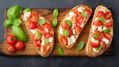 Bruschetta domates, mozzarella peyniri ve fesleğen bir kesme tahtası üzerinde. Geleneksel İtalyan meze veya aperatif, meze. Üstten görünüm. Düz yatıyordu.