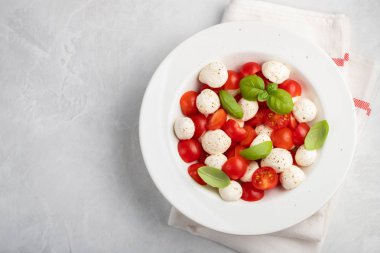 Klasik lezzetli caprese salatası olgun domates, mozzarella ve taze fesleğen ile beyaz tabak gri arka plan üzerinde bırakır. kopya alanı. İtalyan yemeği. Sağlıklı Vejetaryen beslenme kavramı. Üstten görünüm.