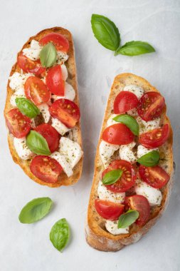 Bruschetta domates, mozzarella peyniri ve fesleğen üzerinde hafif bir arka plan ile. Geleneksel İtalyan meze veya aperatif, meze. Üstten görünüm. Düz yatıyordu.