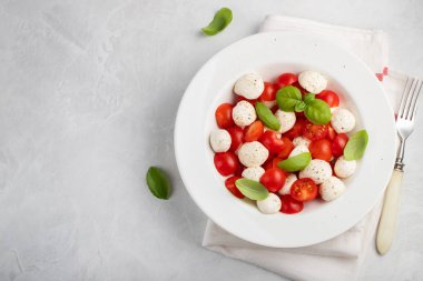 Klasik lezzetli caprese salatası olgun domates, mozzarella ve taze fesleğen ile beyaz tabak gri arka plan üzerinde bırakır. kopya alanı. İtalyan yemeği. Sağlıklı Vejetaryen beslenme kavramı. Üstten görünüm.