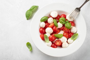 Kopya alanı ile gri arka plan üzerinde beyaz tabak lezzetli caprese salatası olgun domates, mozzarella ve taze fesleğen yaprakları. İtalyan yemeği. Sağlıklı Vejetaryen beslenme kavramı. Üstten görünüm.