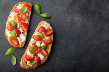 Bruschetta domates, mozzarella peyniri ve fesleğen siyah bir arka plan ile. Geleneksel İtalyan meze veya aperatif, meze. Üstten görünüm kopya alanı ile. Düz yatıyordu