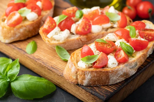 Bruschetta com tomates, queijo mussarela e manjericão em uma tábua de corte. Aperitivo italiano tradicional ou lanche, antipasto — Fotografia de Stock