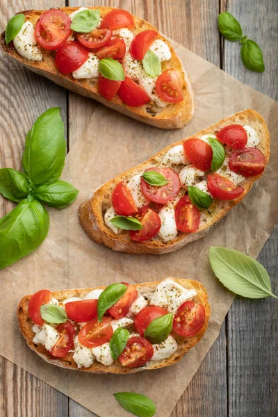 Bruschetta con tomates, queso mozzarella y albahaca sobre una vieja mesa rústica. Aperitivo o merienda tradicional italiana, antipasto. Vista superior. Puesta plana — Foto de Stock