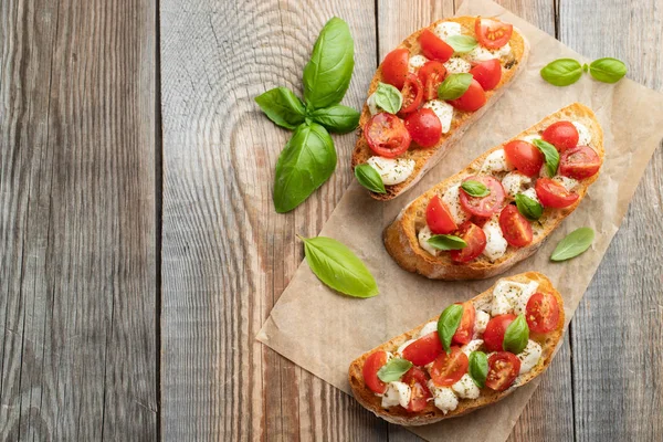 Bruschetta com tomates, queijo mussarela e manjericão em uma velha mesa rústica. Aperitivo italiano tradicional ou lanche, antipasto. Vista superior com espaço de cópia. Depósito plano — Fotografia de Stock