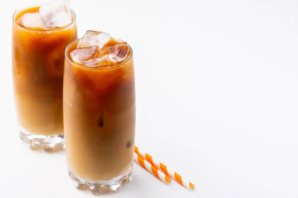 Ice coffee in a tall glass with cream poured over and coffee beans. Cold summer drink on white background with copy space — Stock Photo, Image