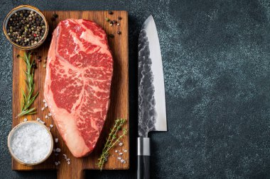 Taze çiğ Başbakan Kara Angus sığır eti biftek ile baharat ahşap tahta üzerinde: Striploin, kaburga. Üstten görünüm kopya alanı ile. Karanlık bir arka plan üzerinde.