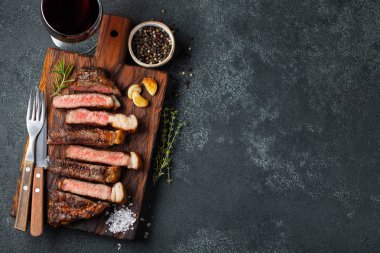 Biber, ızgara biftek Striploin, dilimlenmiş sarmısak, tuz ve kekik bir Ahşap Doğrama tahtası üzerinde karanlık bir taş zemin üzerine kırmızı şarap ile görev yaptı. Kopya alanı ile üstten görünüm.