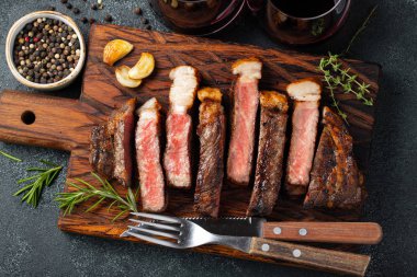 Biber, ızgara biftek Striploin, dilimlenmiş sarmısak, tuz ve kekik bir Ahşap Doğrama tahtası üzerinde karanlık bir taş zemin üzerine kırmızı şarap ile görev yaptı. Üstten görünüm.