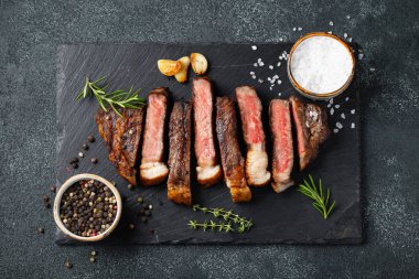 Biber, ızgara biftek Striploin, dilimlenmiş sarmısak, tuz ve kekik mazisi Doğrama Kurulu karanlık bir taş arka plan üzerinde yılları arasında görev yapmıştır. Üstten görünüm.