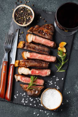 Biber, ızgara biftek Striploin, dilimlenmiş sarmısak, tuz ve kekik mazisi Doğrama Kurulu bir kadeh kırmızı şarap ile karanlık bir taş arka plan üzerinde yılları arasında görev yapmıştır. Üstten görünüm.