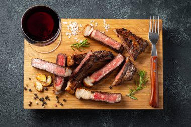 Biber, ızgara biftek Striploin, dilimlenmiş sarmısak, tuz ve kekik bir Ahşap Doğrama tahtası üzerinde karanlık bir taş zemin üzerine kırmızı şarap ile görev yaptı. Üstten görünüm.