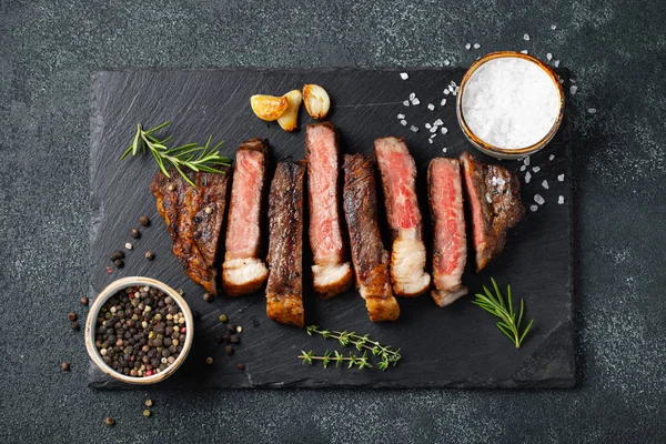 Biber, ızgara biftek Striploin, dilimlenmiş sarmısak, tuz ve kekik mazisi Doğrama Kurulu karanlık bir taş arka plan üzerinde yılları arasında görev yapmıştır. Üstten görünüm.