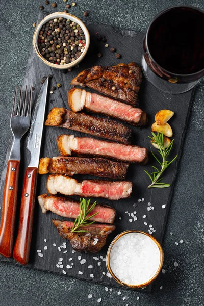 Biber, ızgara biftek Striploin, dilimlenmiş sarmısak, tuz ve kekik mazisi Doğrama Kurulu bir kadeh kırmızı şarap ile karanlık bir taş arka plan üzerinde yılları arasında görev yapmıştır. Üstten görünüm.