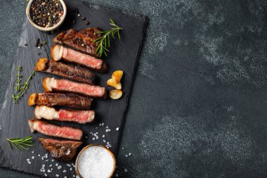 Biber, ızgara biftek Striploin, dilimlenmiş sarmısak, tuz ve kekik mazisi Doğrama Kurulu karanlık bir taş arka plan üzerinde yılları arasında görev yapmıştır. Kopya alanı ile üstten görünüm.