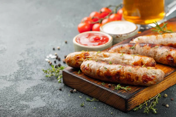 Soslar ve otlar üzerinde ahşap hizmet yönetim kurulu ile kızarmış sosis. Karanlık bir arka plan üzerinde büyük bira Aperatif. Kopya alanı ile.