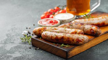 Soslar ve otlar üzerinde ahşap hizmet yönetim kurulu ile kızarmış sosis. Karanlık bir arka plan üzerinde büyük bira Aperatif. Kopya alanı ile