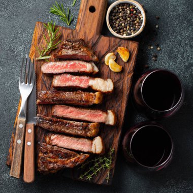 Biber, ızgara biftek Striploin, dilimlenmiş sarmısak, tuz ve kekik bir Ahşap Doğrama tahtası üzerinde karanlık bir taş zemin üzerine kırmızı şarap ile görev yaptı. Üstten görünüm