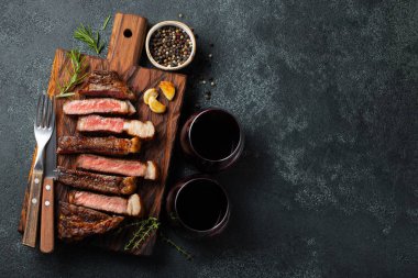 Biber, ızgara biftek Striploin, dilimlenmiş sarmısak, tuz ve kekik bir Ahşap Doğrama tahtası üzerinde karanlık bir taş zemin üzerine kırmızı şarap ile görev yaptı. Kopya alanı ile üstten görünüm