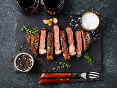 Biber, ızgara biftek Striploin, dilimlenmiş sarmısak, tuz ve kekik mazisi Doğrama Kurulu bir kadeh kırmızı şarap ile karanlık bir taş arka plan üzerinde yılları arasında görev yapmıştır. Üstten görünüm