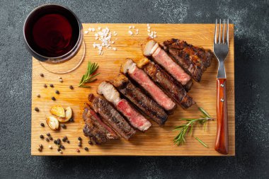 Biber, ızgara biftek Striploin, dilimlenmiş sarmısak, tuz ve kekik bir Ahşap Doğrama tahtası üzerinde karanlık bir taş zemin üzerine kırmızı şarap ile görev yaptı. Üstten görünüm