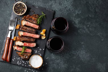 Biber, ızgara biftek Striploin, dilimlenmiş sarmısak, tuz ve kekik mazisi Doğrama Kurulu bir kadeh kırmızı şarap ile karanlık bir taş arka plan üzerinde yılları arasında görev yapmıştır. Kopya alanı ile üstten görünüm