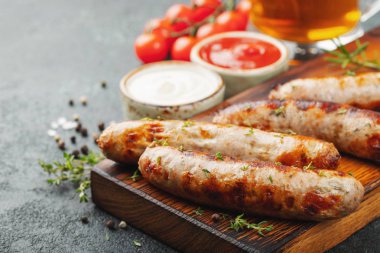 Soslar ve otlar üzerinde ahşap hizmet yönetim kurulu ile kızarmış sosis. Büyük bira Aperatif karanlık bir arka plan üzerinde.