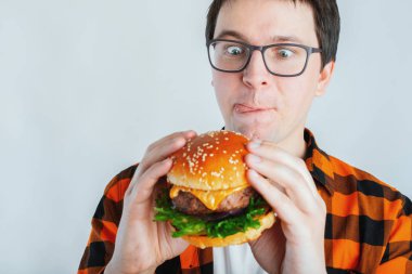 Hamburger bir parçası tutan genç adam. Öğrenci fast food yiyor. Burger yararlı yemek değil. Çok aç adam burger bakıp dudaklarını yalıyor. Diyet kavramı. Kopya alanı ile metin için.