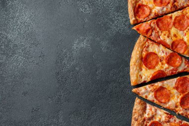 Dilimleri lezzetli taze pizza sosis sucuk ve peynir ile karanlık bir arka plan üzerinde kesmek. Üstten görünüm metin için kopya yer ile. Pizza siyah beton masada. düz lay