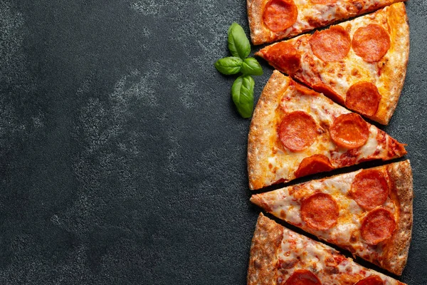 In Scheiben geschnitten köstliche frische Pizza mit Wurst-Peperoni und Käse auf dunklem Hintergrund. Ansicht von oben mit Kopierraum für Text. Pizza auf dem schwarzen Betontisch. flache Lage — Stockfoto