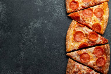 Dilimleri lezzetli taze pizza sosis sucuk ve peynir ile karanlık bir arka plan üzerinde kesmek. Üstten görünüm metin için kopya yer ile. Pizza siyah beton masada. düz lay.