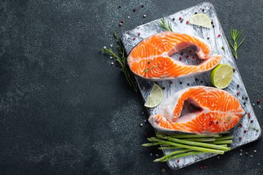 İki ham taze somon veya alabalık biftek buz, kireç, kekik ve karanlık bir arka plan üzerinde genç kuşkonmaz ile omega-3 yağ açısından zengin. Sağlıklı ve diyet gıda. Üstten görünüm kopya alanı ile. Düz yatıyordu.