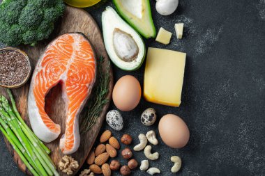 Karanlık bir arka plan keto diyet için sağlıklı gıda kümesi. Keten tohumu, brokoli, avokado, tavuk yumurta, fındık ve bir ahşap tahta üzerinde kuşkonmaz ile taze çiğ somon biftek. Kopya alanı ile üstten görünüm.